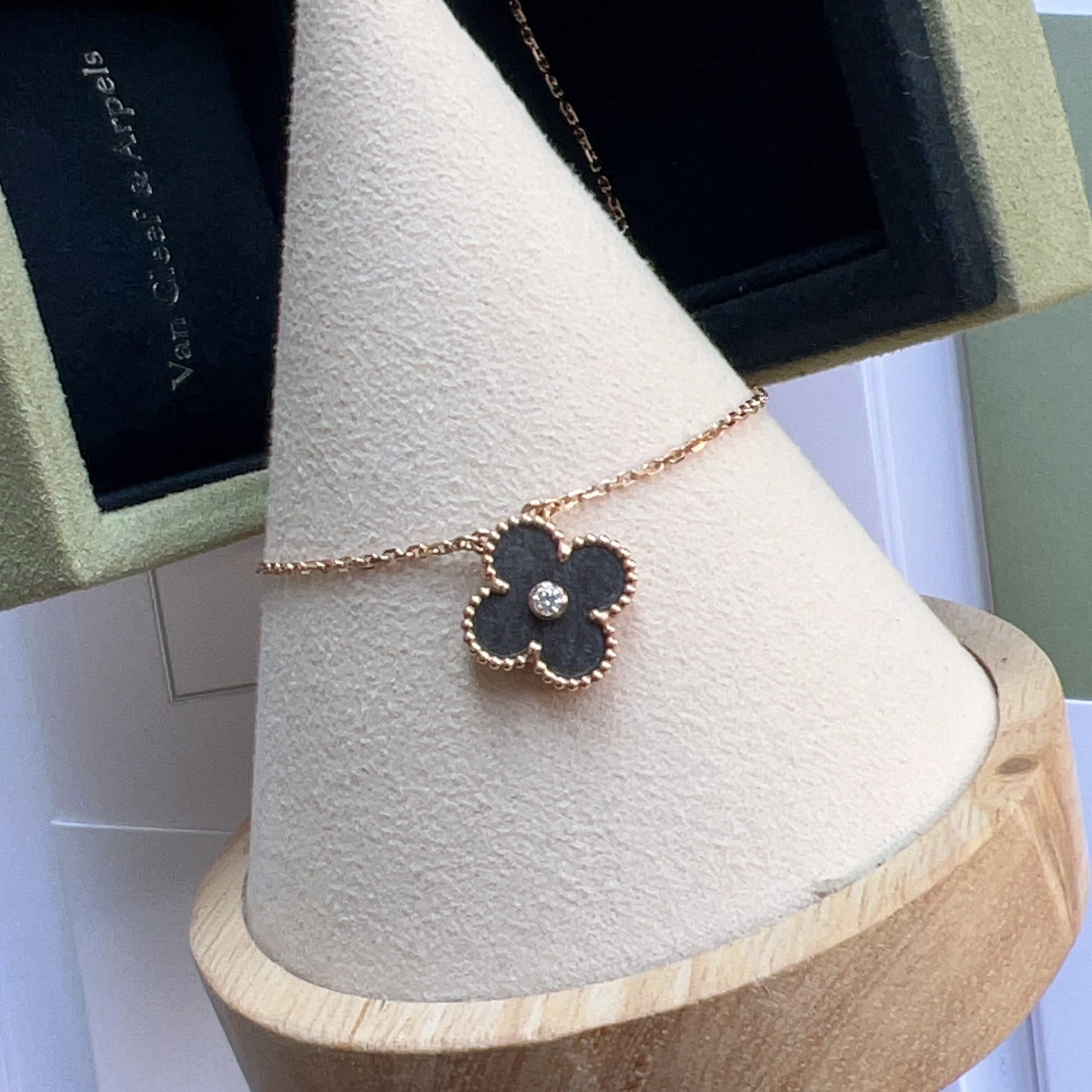 Black flower-shaped earring on a wooden display stand with a green jewelry box in the background.