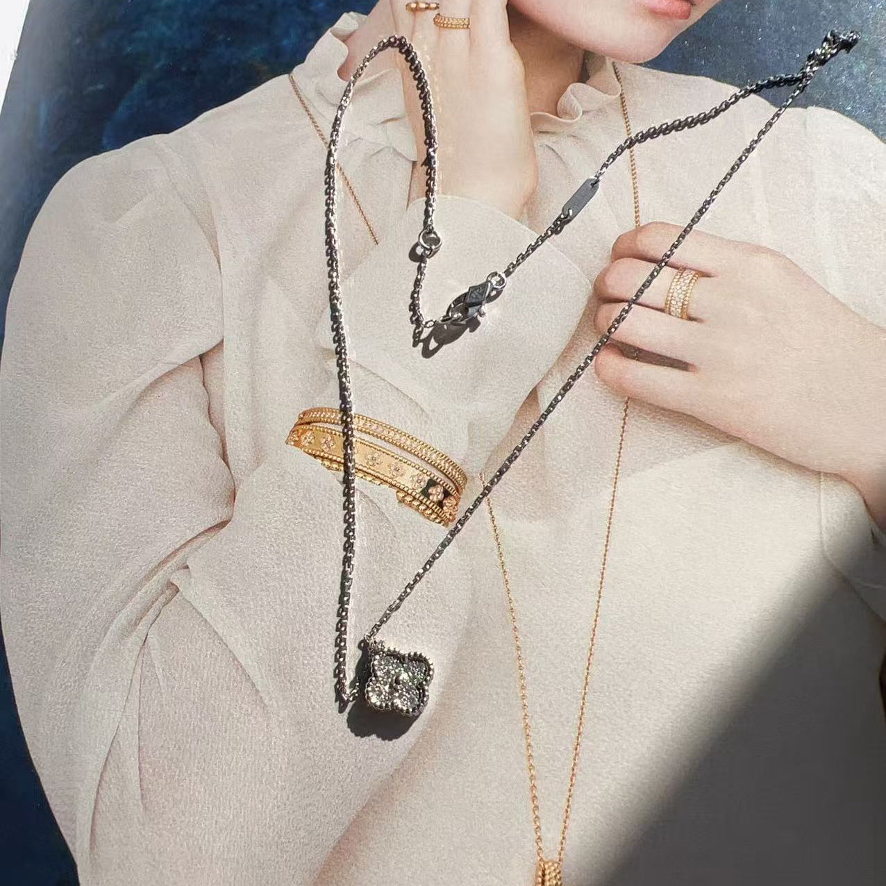 Person wearing a beige outfit with jewelry including necklaces and rings.