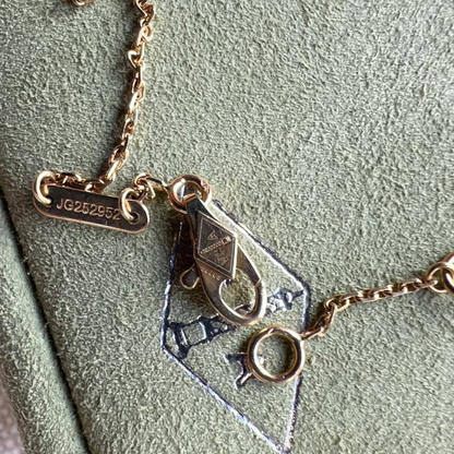 Gold necklace with geometric pendant on a green surface