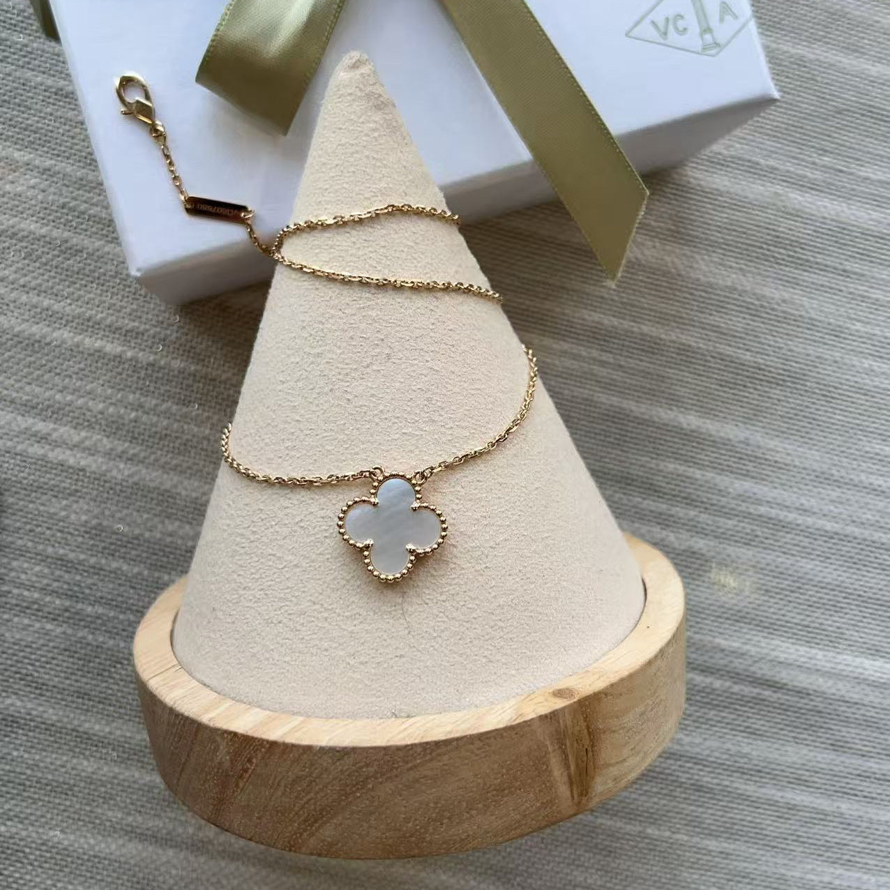 Necklace with a clover-shaped pendant on a wooden stand, with a gift box in the background.