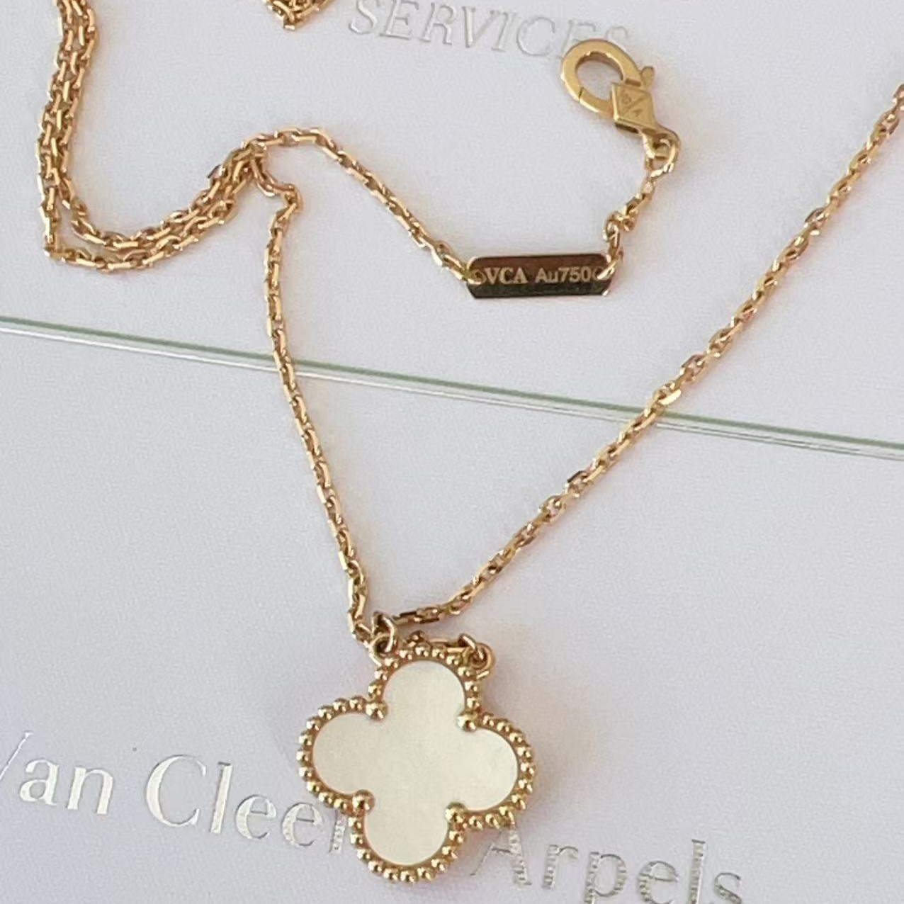 Gold necklace with a white pendant on a light gray background