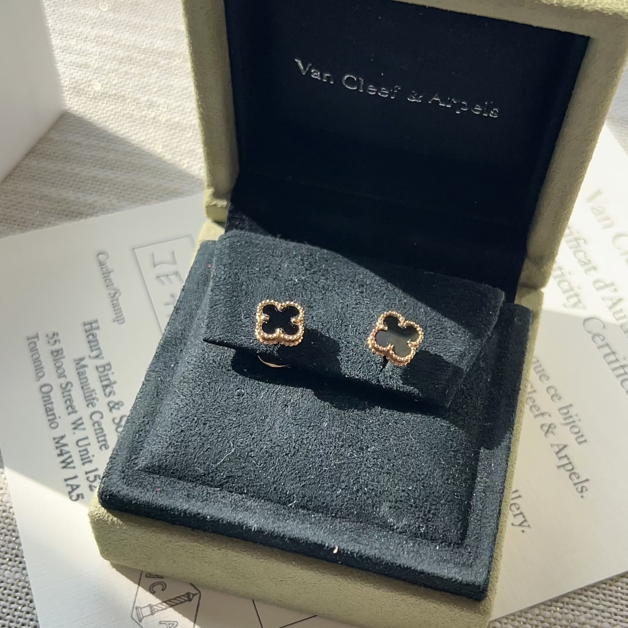 Gold clover-shaped earrings in a Van Cleef & Arpels box on a textured surface.
