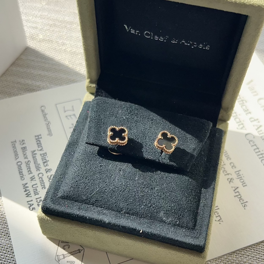 Gold clover-shaped earrings in a Van Cleef & Arpels box on a textured surface.