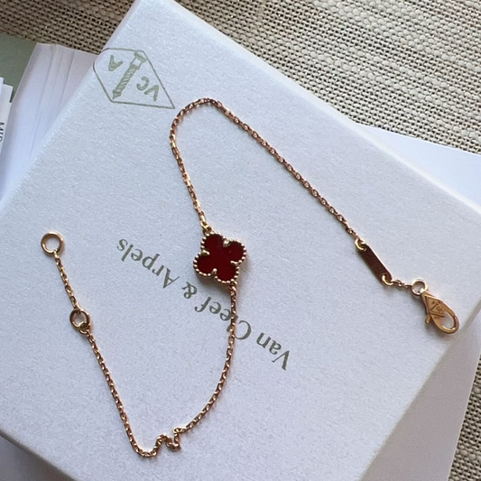 Gold necklace with a red flower pendant on a Van Cleef & Arpels box.