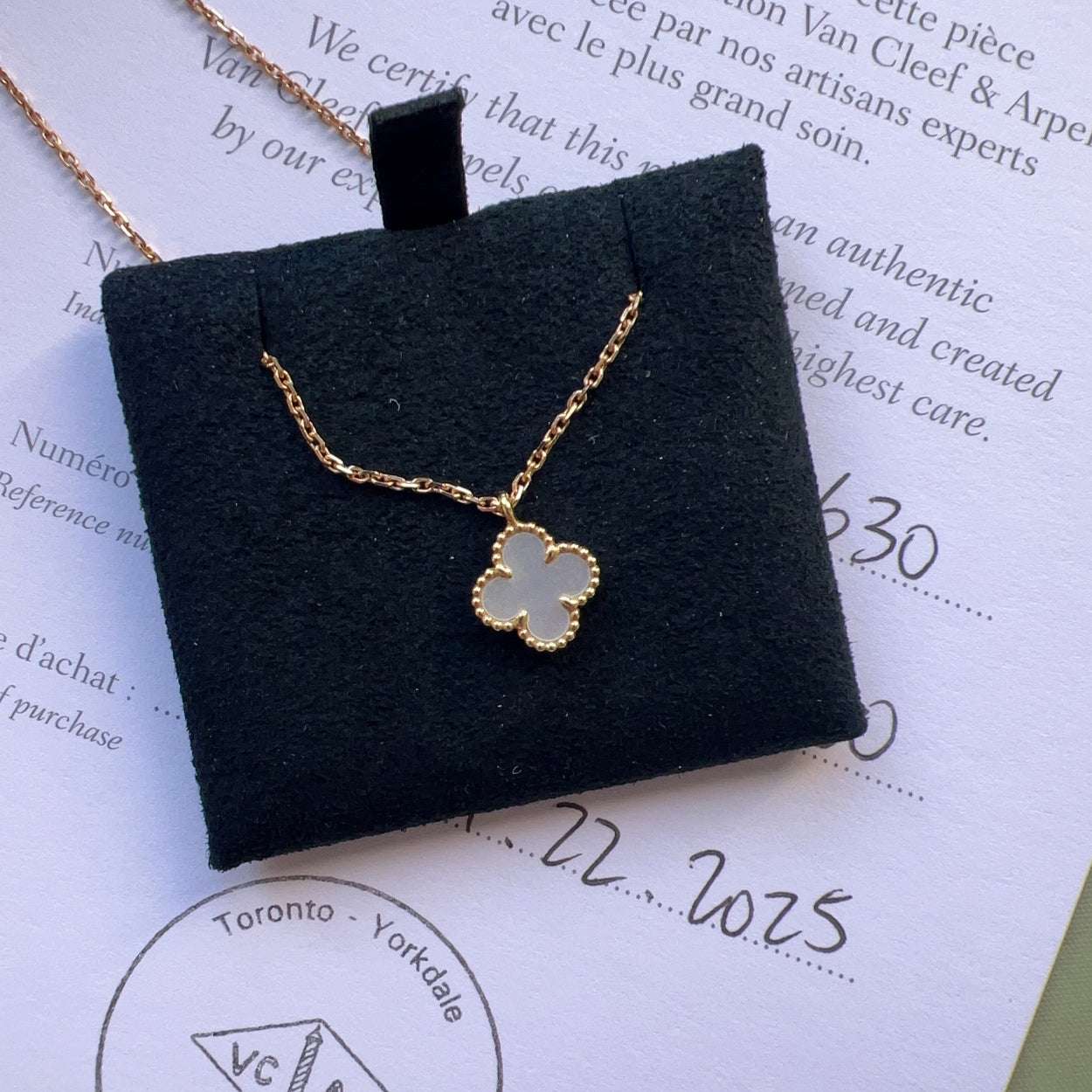 Gold necklace with a clover pendant on a Van Cleef & Arpels box with certification text.