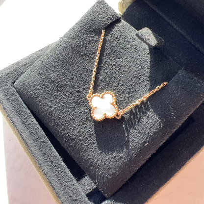 A rose gold necklace with a clover-shaped pendant featuring a white inlay, displayed on a black velvet jewelry box.