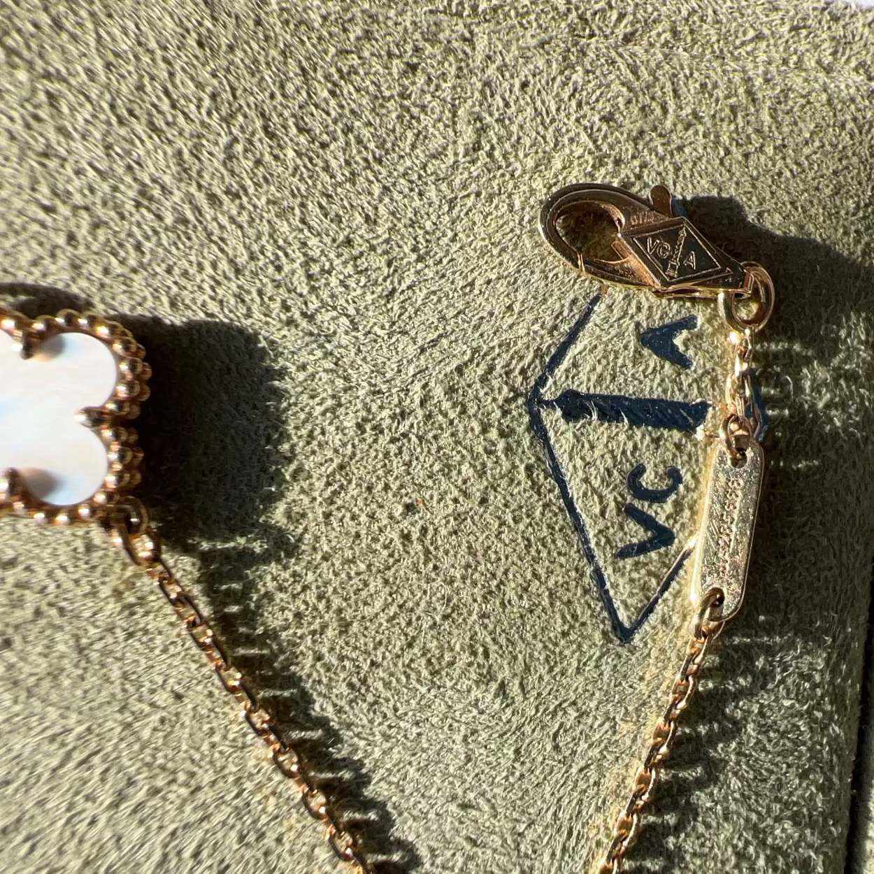 Close-up of a gold-tone jewelry clasp and chain attached to a textured olive-green jewelry box, with part of a flower-shaped charm visible on the left.