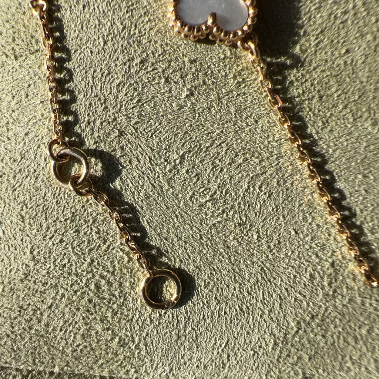 Close-up of a gold-toned chain necklace with a small interlocking rings clasp and a circular ring extender, laid on a textured light green jewelry display surface.