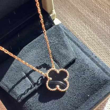 A rose gold four-leaf clover pendant necklace on a matching chain, displayed on a black velvet jewelry box.